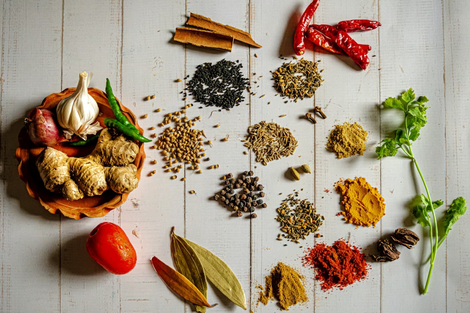 An assortment of whole spices, seeds and seasonings on a warm wooden surface